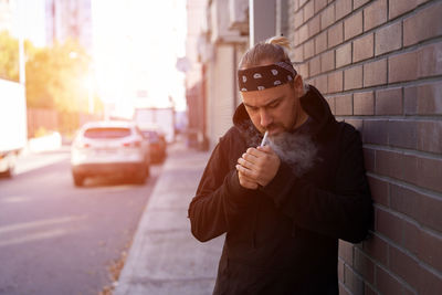 Man smoking cigarette while standing on sidewalk in city
