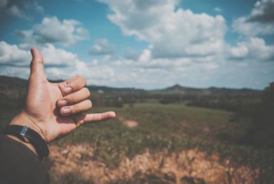 Midsection of person hand on field against sky