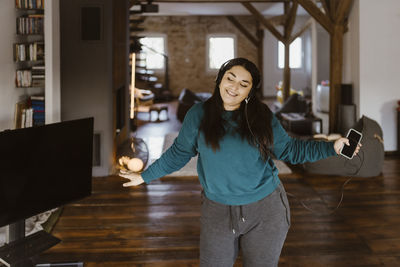 Woman dancing in living room while listening to music at home