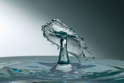 Close-up of drop falling on glass against white background