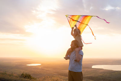 Happy man and little boy, father and sons, with kite in nature at sunset