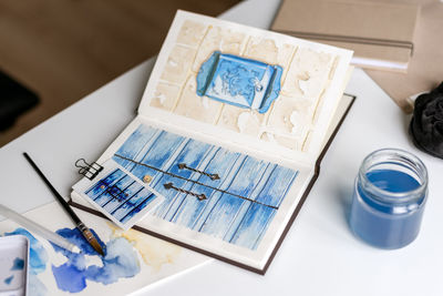 An open watercolor sketchbook lies on a white table.