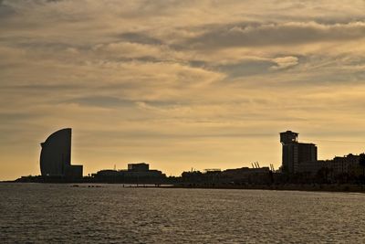 Silhouette buildings by sea against sky during sunset