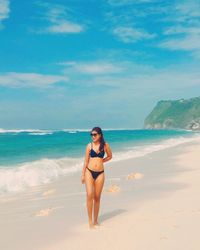 Full length of woman in bikini standing on beach against sky