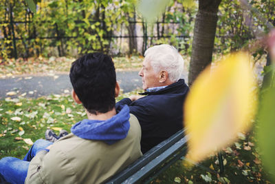 Caretaker and senior man sitting on bench at park