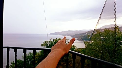 Close-up of hand by sea against sky