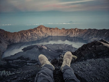 Low section of person on rock in mountains against sky