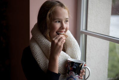 Teenage girl having coffee while sitting by window at home