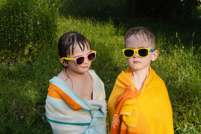 Wet children in sunglasses in a towel. smiling girl looks away, serious boy forward. 