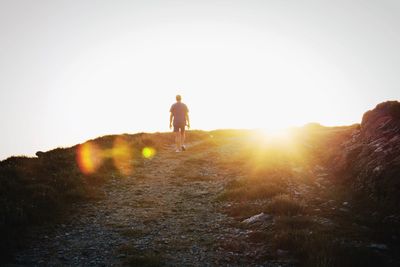 Rear view of man walking on dirt road against sunset sky