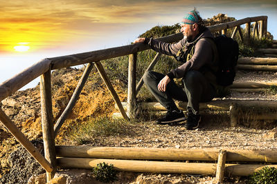 Full length of young man sitting against sky during sunset