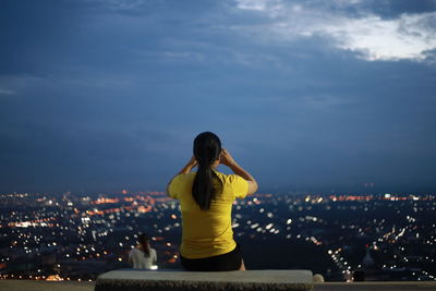 Rear view of woman looking at illuminated city against sky