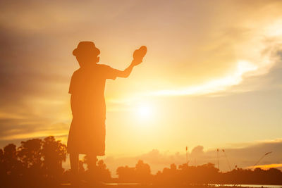 Silhouette man standing on field against sky during sunset