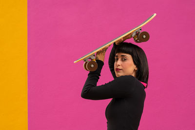 Beautiful woman with short hair posing with a skateboard on a colored background