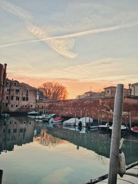 Buildings by river against sky at sunset