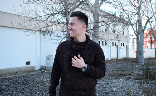 Young man looking away while standing on bare tree