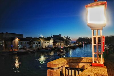 Illuminated buildings by canal against blue sky at night