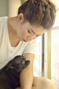 Young woman petting dog while sitting on window at home