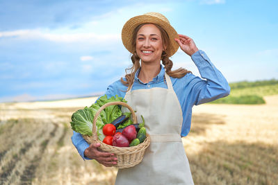 Portrait of smiling young woman standing in basket on field