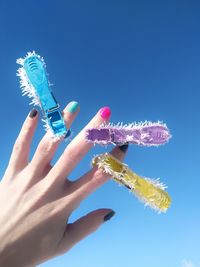 Cropped hand of woman wearing colorful clothespin against sky