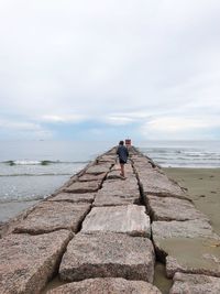 Man standing on rock at beach against sky