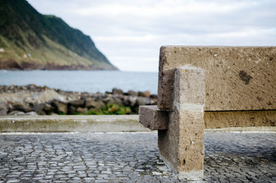 Empty stone bench by sea against sky