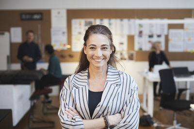 Portrait of smiling businesswoman with colleagues in background at creative office