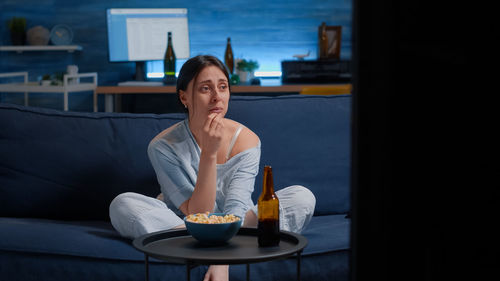 Young woman looking away while sitting on sofa