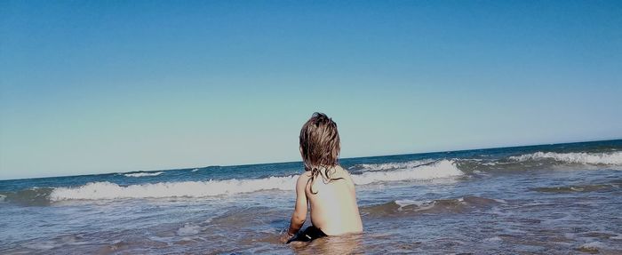 Rear view of woman on beach against clear sky