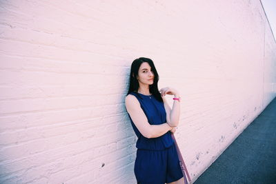 Portrait of young woman standing against wall