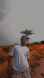 Portrait of young man standing on field against sky