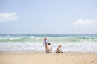 Siblings playing at beach against sky during sunny day