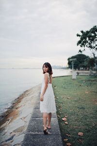 Portrait of young woman standing by sea against sky