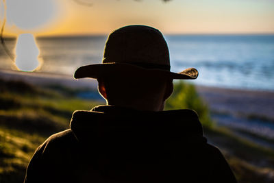 Rear view of man looking at sea against sunset sky