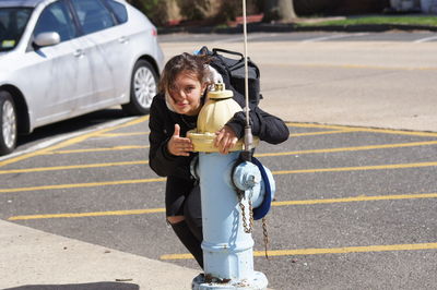 Portrait of teenage girl holding fire hydrant on road