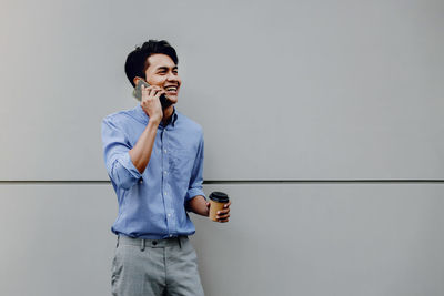 Smiling girl holding mobile phone standing against wall