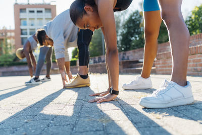 Young sportswoman practicing exercise by friends on footpath