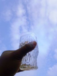 Cropped image of hand holding drink against sky