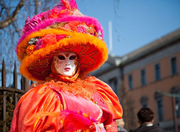 Portrait of woman in costume and mask during carnival standing against sky in city