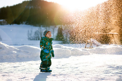 Young boy in farm watching snow fall in winter wonderland on sunny day