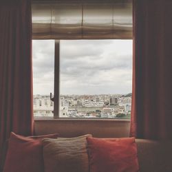 Cityscape against sky seen through glass window of living room