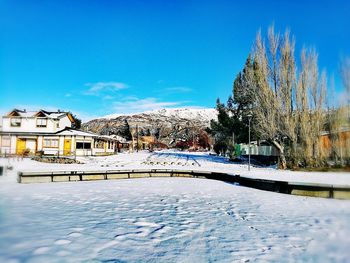 Bare trees by frozen lake against clear blue sky