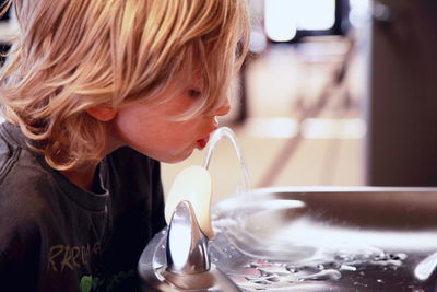 Side view of cute boy drinking water from fountain