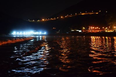 Illuminated buildings by sea against sky at night