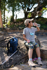 Full length of girl drinking water while sitting on rock