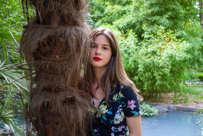 Portrait of woman standing by tree trunk