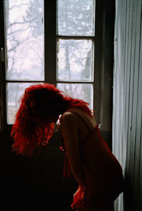 Side view of woman with redhead bending by window