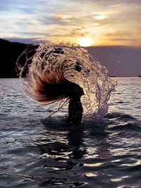 Horse in sea against sunset sky