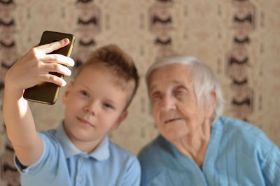 Happy elderly 90-year-old woman with gray hair wearing a jacket and her grandsone using a smartphone