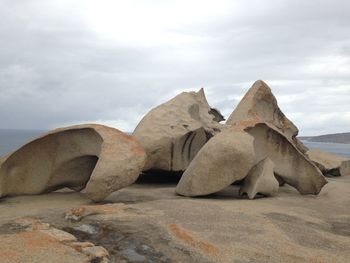 Rocks on sand at beach against sky